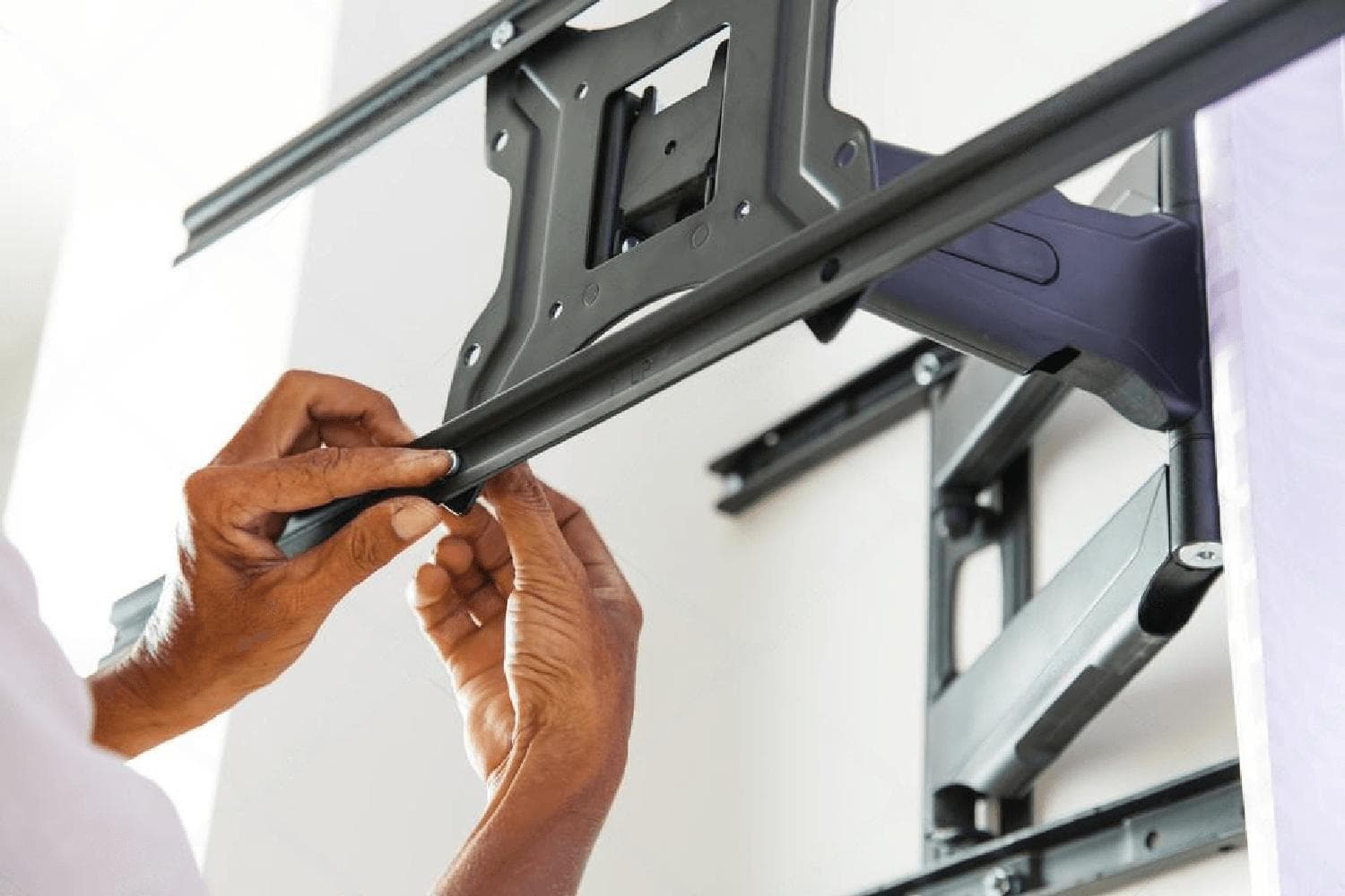 Technician's hands securing a full-motion TV wall-mount bracket to the wall during installation.